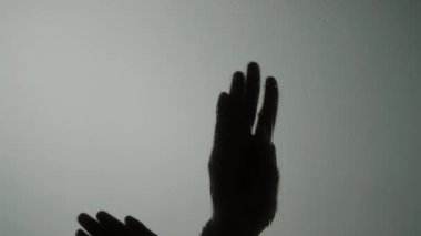 Ellerin gölgesinin yakın görüntüsü ıslak duş kabini camının arkasında düzgün hareketler yapıyor.
