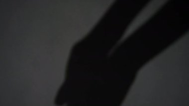 Gri arkaplanda birbirine dolanan ve aşağıya doğru yönelen odaksız uzun el gölgesinin yakın görüntüsü
