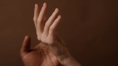 Erkek elinin kadın eline uzandığı ve yavaşça parmaklarına ve avucuna dokunduğu kahverengi duvar kağıdının yakın görüntüsü.