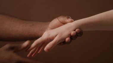 Tanımlanamayan siyah bir adamın beyaz bir kadının elini tutarak kahverengi duvar kağıdına şefkatle dokunuşunun detaylı görüntüsü.