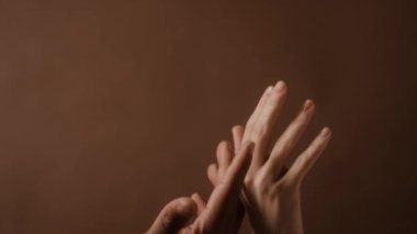 Beyaz bir kadının, kahverengi duvar kâğıdına dokunup elini sıvazladığı arka avucunun görüntüsü.