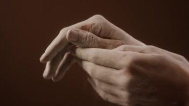 Kadın elinin, kahverengi duvar kağıdına kurumuş beyaz kil sürtünmesinin detaylı görüntüsü.