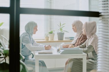 Tıp bürosundaki üç kadın, cam kenarında saksıda saksılarla oturup sağlık hizmetleri uzmanlarının iletişim kurduğu sakin bir ortam yaratarak sağlık sorunlarını tartışıyor.