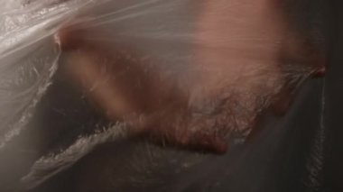 Plastik filmin arkasındaki kimliği belirsiz kişinin parmaklarıyla dokunup gerdiği yakın plan görüntüsü.