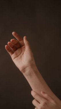 Bilinmeyen kadının dikey ayrıntılı görüntüsü kahverengi arka planda avuç içi, bilek ve ön kol üzerinde nazikçe çalışan parmaklar.