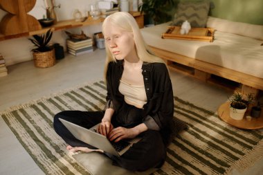 Z jenerasyonunun albinizmli kadın yazarı rahat oturma odasında yerde oturuyor ve sabahları dizüstü bilgisayarla çalışıyor.