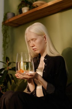 Küçük bir akvaryumu elinde tutan ve Japon balığına bakan albinizmle Z jenerasyonunun dikey görüntüsü.