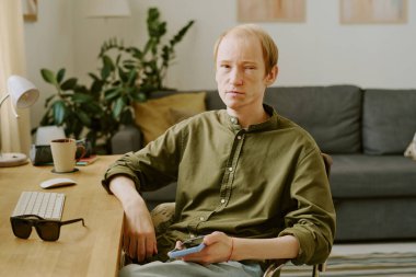 Kafkasyalı engelli bir adamın portresi ahşap masada oturuyor ve elinde akıllı telefon var.