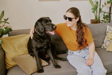 Özürlü genç bir kadın oturma odasında rahat bir kanepede dinlenirken sadık köpeğine sarılıyor.