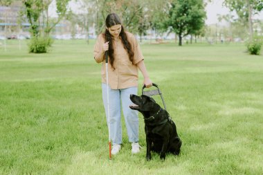Siyah Labrador 'u ona bakarken elinde metal baston ve rehber köpek tasması tutan esmer kadın.