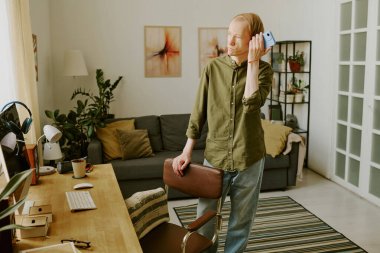 Özürlü bir adam oturma odasında çalışma alanlarının yanında dururken ses dinliyor.