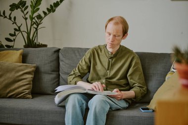 Kafkasyalı engelli bir adam evde otururken Braille kitabı okumaktan zevk alıyor.