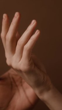 Güçlü erkek elinin dikey detaylı çekimi zarif bir kadın avucunun kahverengi arka planına dokunuyor.