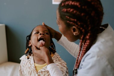 Doktorların muayenehanesinde çocukların boğazını muayene eden, sağlık kontrolüne odaklanan ve genç bir hastanın rahatını sağlayan tıbbi uzmanlar.