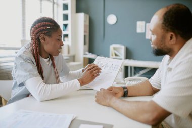 Hastaya danışmanlık yapmak, klinik odasında raflar ve arka planda kitaplarla tıbbi kayıtları tartışmak.