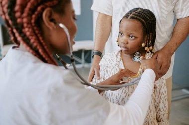 Klinikteki genç kızın muayenesi sırasında steteskop kullanan bir tıp uzmanı, sağlık değerlendirmelerinde konsantrasyon ve eksiksizlik göstermektedir.