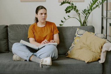 Genç, ciddi bir kadın evde vakit geçirirken Braille kitabı okuyor.