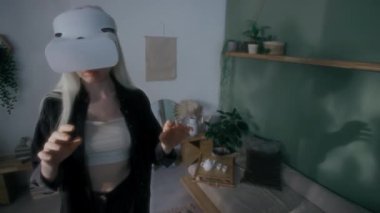 Beyaz bluzlu, siyah tişörtlü, ayakta duran ve evde vr kulaklık kullanarak oyun oynayan albino kızın yukarıdan görüntüsü