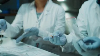 Tek kullanımlık eldivenler ve beyaz önlüklü siyah bir adli tıp uzmanı kanıt torbasından mermiyi çıkarıyor ve bunu suç laboratuarında birlikte çalışırken melez bir kadın meslektaşla tartışıyor.