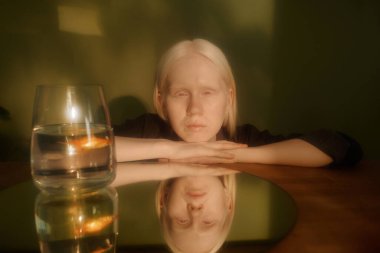 Unusual girl with albinism posing for portrait with mirror reflection and goldfish in aquarium in warm morning light clipart