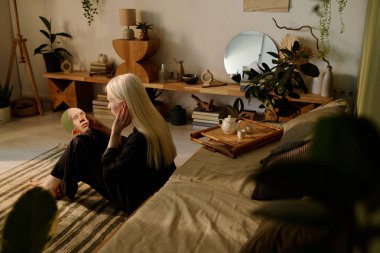 Geniş açıda, albinizmli genç bir kadın yerde oturmuş aynaya bakıyor, boşluğu kopyalıyor.