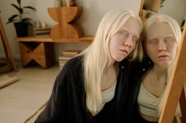 Albinizmli genç bir kadının kavramsal portresi yerde oturuyor ve aynaya yaslanıyor gözleri kapalı, boşluğu kopyalıyor.