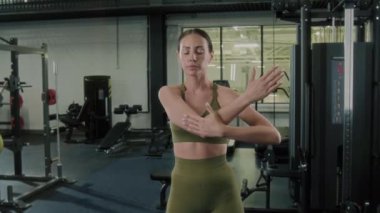 Spor sutyenli ve taytlı genç bir kadın çapraz vücut omuzu ve üst kol kasları esnetiyor.