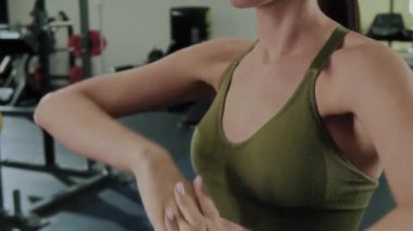 Spor sutyenli genç bir kadının spor salonunda egzersiz öncesi ısınma sırasında bilek dalgaları ve rotasyonları yapmasını yakından izle.