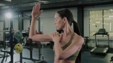 Spor giyimli genç bir kadın spor salonunda antrenman yaparken omuz hareketi egzersizi yapıyor.