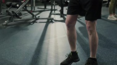 Spor kıyafetleri giymiş güçlü bir adamın spor salonunda ip atlama egzersizi yaparken, antrenmana devam etmeden önce kısa bir ara verirken çekilen çekim.
