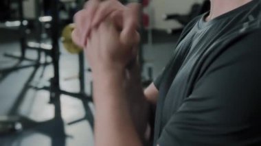 Spor giyimli, spor giyinmiş, spor salonunda duran ve bilek döndürme egzersizi yapan tanınmamış bir adamın ellerini kapalı tut.