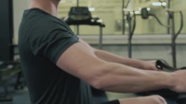 Spor salonunda egzersiz yaparken erkek sporcunun sıralı makineye kablo çektiği orta bölüm çekimi.