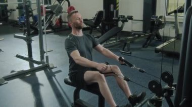 Spor giyim sektöründe formda bir adam spor salonunda kürek çekme makinesinde kablolu yayında güç ve dayanıklılık eğitimine odaklanıyor.