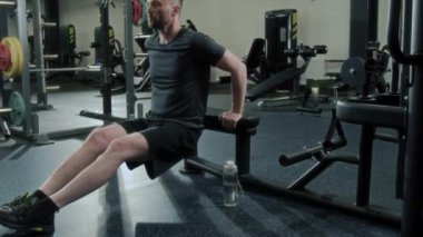 Spor kıyafetli kaslı adam spor salonunda antrenman yaparken yedek kulübesinde dalış yapıyor.