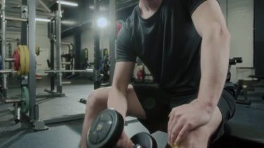 Spor kıyafetli bir adamın spor salonunda ağırlık antrenmanı sırasında tek kollu halter kıvrımı egzersizi yaparken görüntüsünü kaldır.