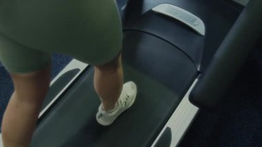 Spor salonunda kardiyo ve dayanıklılık eğitimi sırasında koşu bandında koşan atletik bir kadının bacaklarının üstünden yakından bakın.