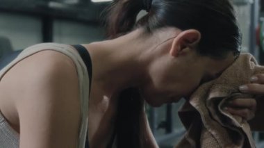 Yorgun bir kadın yoğun spor salonundan sonra yüzünü havluyla siliyor.