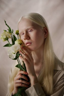 Beyaz Eustoma çiçekleri ile kameraya poz veren beyaz tenli genç beyaz kadının dikey yakın çekim stüdyo portresi.