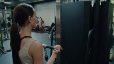 Spor kıyafetli genç bir kadın spor salonunda spor salonunda güç antrenmanı sırasında biseptik kablo kıvrımları yapıyor.