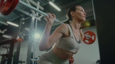 Düşük açılı, formda genç bir kadının ağırlık kaldırma hareketleri. Sonra spor yaparken halteri askıya takması.