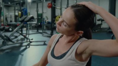 Genç bir kadın spor salonundan sonra kaslarını gevşetip boynunu esnetiyor ve yan büküyor.