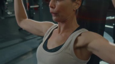 Spor kıyafetli güçlü bir kadının spor salonundaki halterleri kaldırışını spor salonu antrenmanı sırasında omuz presi yaparken görüntüsünü kapatın.