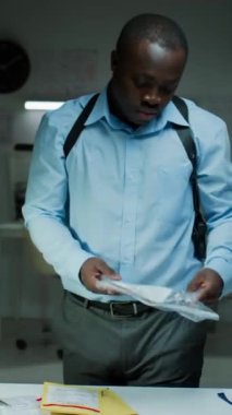 Siyahi araştırmacının delilleri analiz ederken dikey portresi. Sonra da adli tıp laboratuarındaki kameraya rahatça poz veriyor.