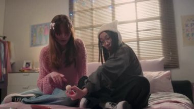 İki kız arkadaş liçi yer ve yatakta otururken akıllı telefondan K-pop müzik videosu izlerler.