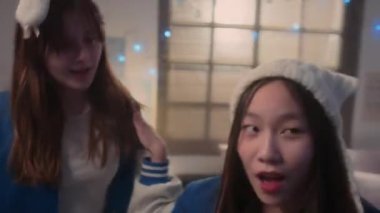 Aynı kıyafetleri giymiş, K-pop şarkısıyla dans eden ve kameraya bakan iki liseli kızın görüntüsünü büyüt.