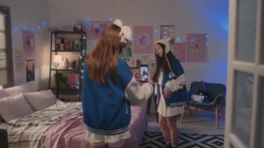 Genç kız, Asyalı okul arkadaşının yatak odasında K-pop dansı yaptığı akıllı telefonuyla video kaydediyor.