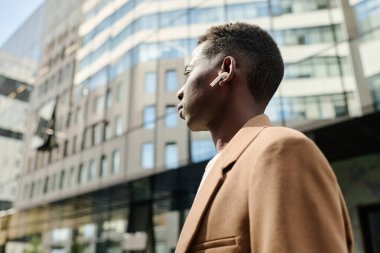 Düşük açılı orta ölçekli, işe giderken müzik dinleyen, kablosuz kulaklık takan siyahi bir adamın fotoğrafı.