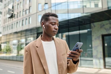 Modern iş bölgesinde açık havada duran Z Gen Siyah adam işe giderken akıllı telefondan çalma listesini değiştiriyor.