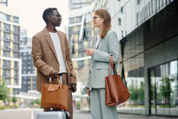 Молодой афро-американский генеральный директор встречается со своей коллегой-кавказкой в деловой поездке, они стоят на улице и разговаривают