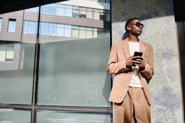 Güneş gözlüğü ve kulaklık takmış, güneşli bir yaz gününde açık havada müzik dinleyen Afrikalı genç bir menajerin düşük açılı görüntüsü.